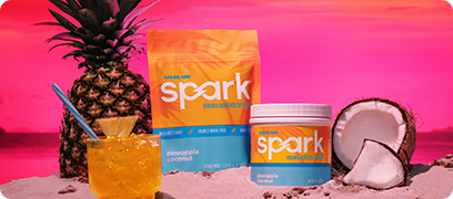 Spark Pineapple Coconut Gusset Bag and Canister sitting on a beach surrounded by a pineapple and coconut along with a mixed Spark Pineapple Coconut drink.