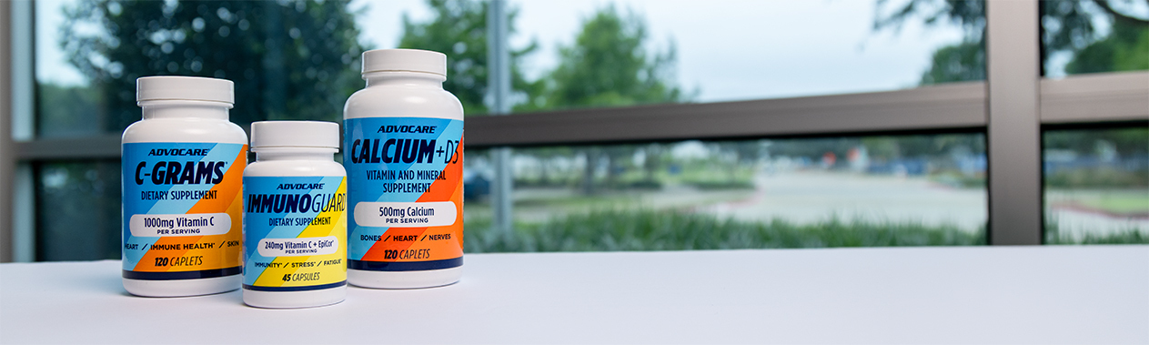 AdvoCare C-Grams, ImmunoGuard and Calcium + D3 bottles on a desk in front of a window.