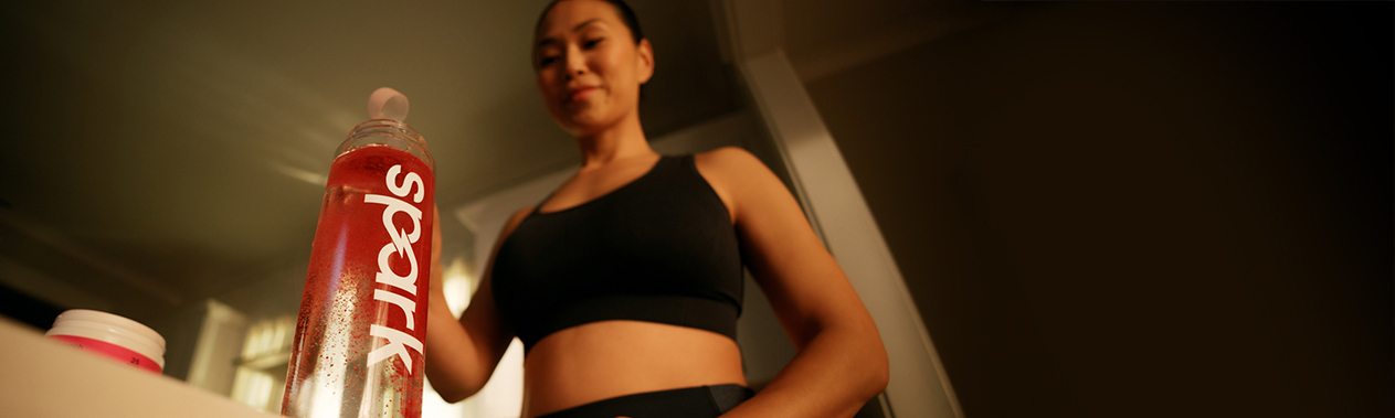 A woman in workout clothes pouring Spark® into a clear Spark® labeled bottle of water.