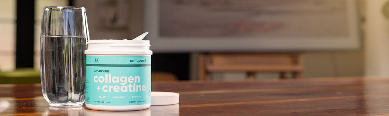 A canister of Collagen + Creatine sitting on a wood dining room table next to a glass of water.