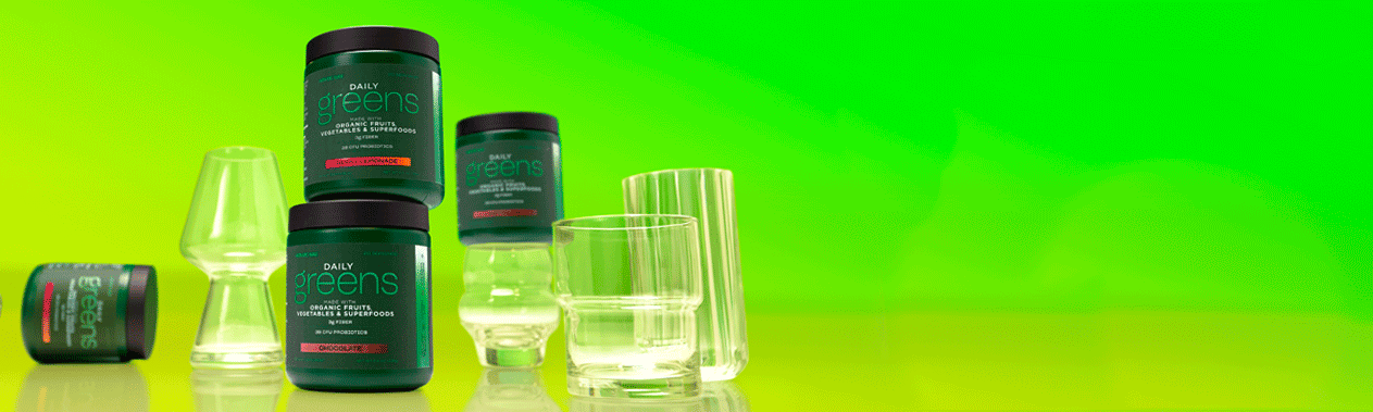 AdvoCare Daily Greens canisters stacked next to empty drinking glasses on a green background.