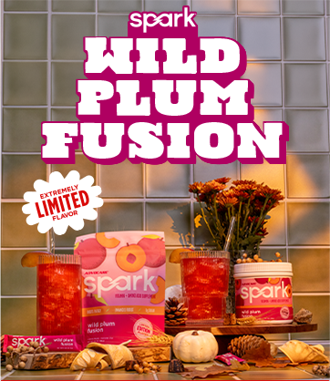 Extremely Limited Flavor Spark Wild Plum Fusion. Spark Wild Plum Fusion canister and stick pack on a kitchen counter top surrounded by fall flowers and glasses with mixed drinks.